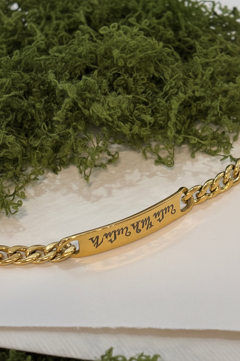 Bracciale personalizzato in acciaio dorato con piastrina incisa a laser nell'alfabeto Theban, indossato al polso
