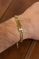 Bracciale personalizzato in acciaio dorato con piastrina incisa a laser nell'alfabeto Theban, indossato al polso