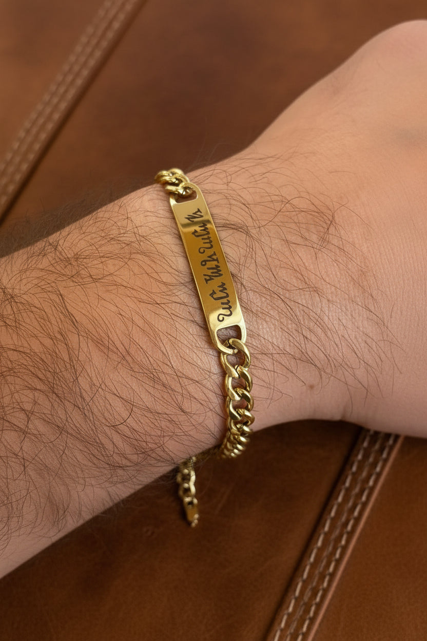Bracciale personalizzato in acciaio dorato con piastrina incisa a laser nell'alfabeto Theban, indossato al polso