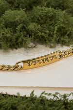 Bracciale personalizzato in acciaio dorato con piastrina incisa a laser nell'alfabeto Theban, indossato al polso