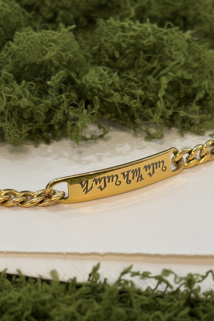 Bracciale personalizzato in acciaio dorato con piastrina incisa a laser nell'alfabeto Theban, indossato al polso